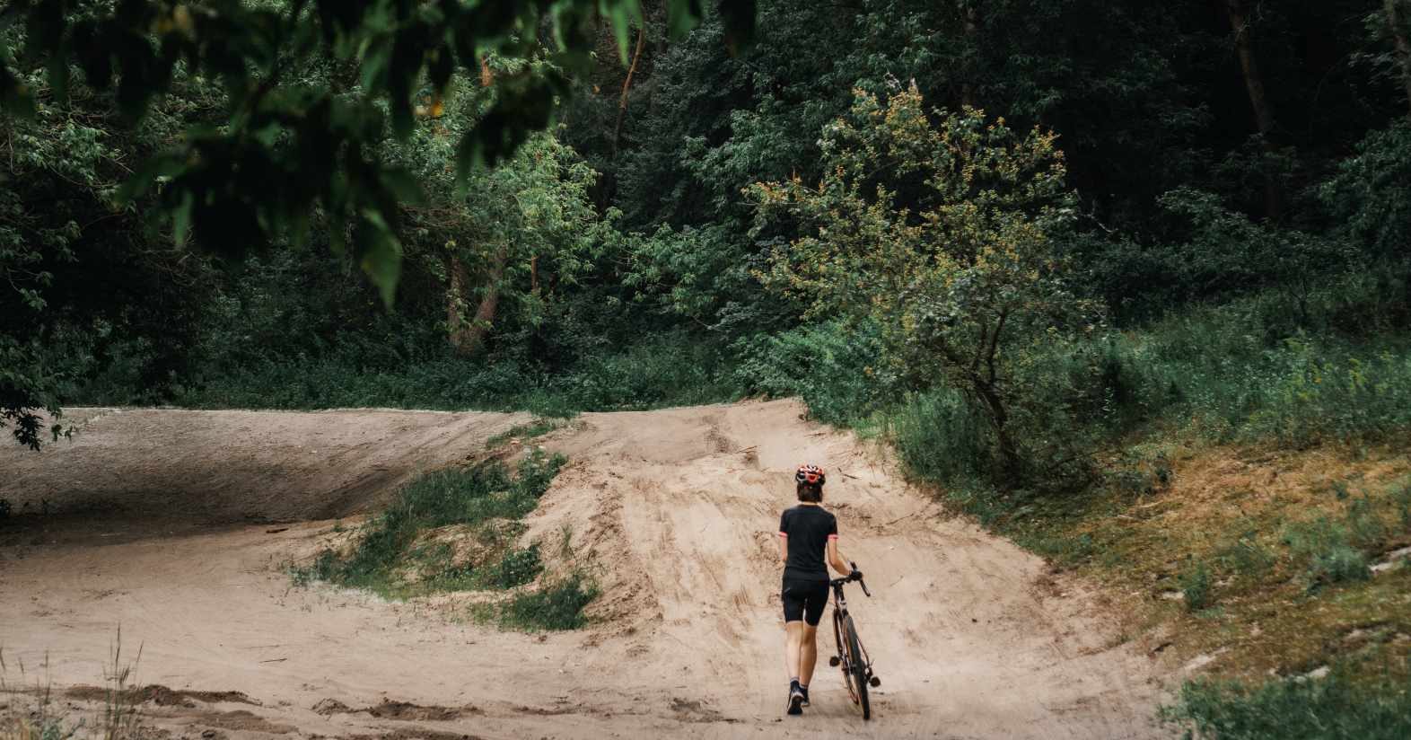 A woman walks along a trail pushing her bike